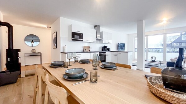 Une cuisine moderne avec des meubles blancs, un four à micro-ondes et un coin repas doté d’une table en bois, mise pour quatre personnes.