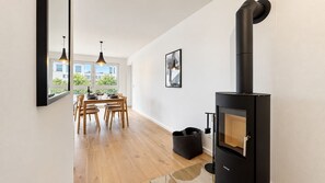 A modern kitchen with a wood-burning stove, a dining area with wooden chairs, and a large window providing a view of the outside. - Vacation apartment in the mountain resort 3.3.5 - Adventure & wellness with infrared cabin! (Winterberg)