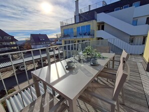 Un balcon avec une table dressée pour deux personnes, un pot de fleurs et une vue dégagée sur le quartier environnant.
