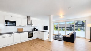 A modern kitchen with white cabinetry, a built-in oven, and a large window overlooking a residential area. - Vacation Apartment in a Mountain Resort 3.3.5 - Adventure & Wellness with an Infrared Sauna! (Winterberg)