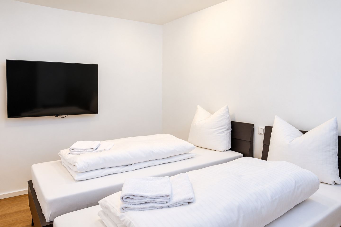 Une chambre d’hôtel avec deux lits, un téléviseur à écran plat fixé au mur et un plancher en bois.