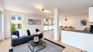 A modern living room with a sofa, a coffee table, and a dining area with a kitchen counter. - Vacation apartment in the mountain resort 3.3.5 - Adventure & wellness with infrared cabin! (Winterberg)