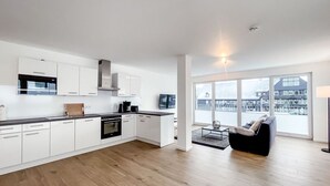 A modern kitchen with white cabinets, a black countertop, and a large window offering a view of buildings. - Vacation apartment in the mountain resort 3.3.5 - Adventure & wellness with infrared cabin! (Winterberg)