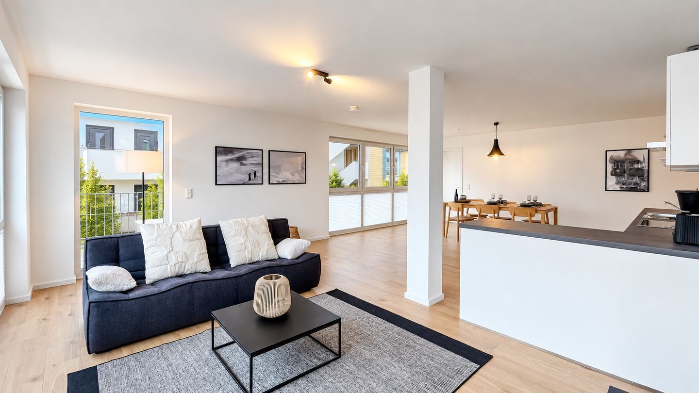 A modern living room with a sofa, a coffee table, and a dining area with a kitchen counter.