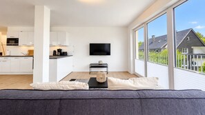 A modern living room with a grey sofa, a flat-screen TV, and a kitchen in the background. - Vacation apartment in the mountain resort 3.3.5 - Adventure & wellness with infrared cabin! (Winterberg)