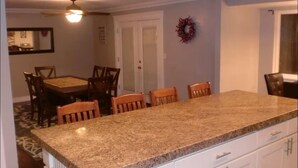 A kitchen with granite countertops, wooden chairs, a dining table, and a ceiling fan.