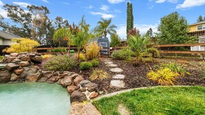 A backyard with a swimming pool, a stone pathway, and various plants. - Tranquil Retreat: Pool, Spa, Firepit, Peloton, WFH (Orangevale)