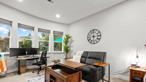A modern office space with a desk, two monitors, a leather chair, a clock, and a window with a view of greenery. - Tranquil Retreat: Pool, Spa, Firepit, Peloton, WFH (Orangevale)