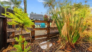 A wooden fence with a gate, a small garden area with various plants, and a glimpse of a house in the background. - Tranquil Retreat: Pool, Spa, Firepit, Peloton, WFH (Orangevale)