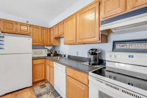 A kitchen with wooden cabinets, a white refrigerator, a microwave, a coffee maker, and a stove.