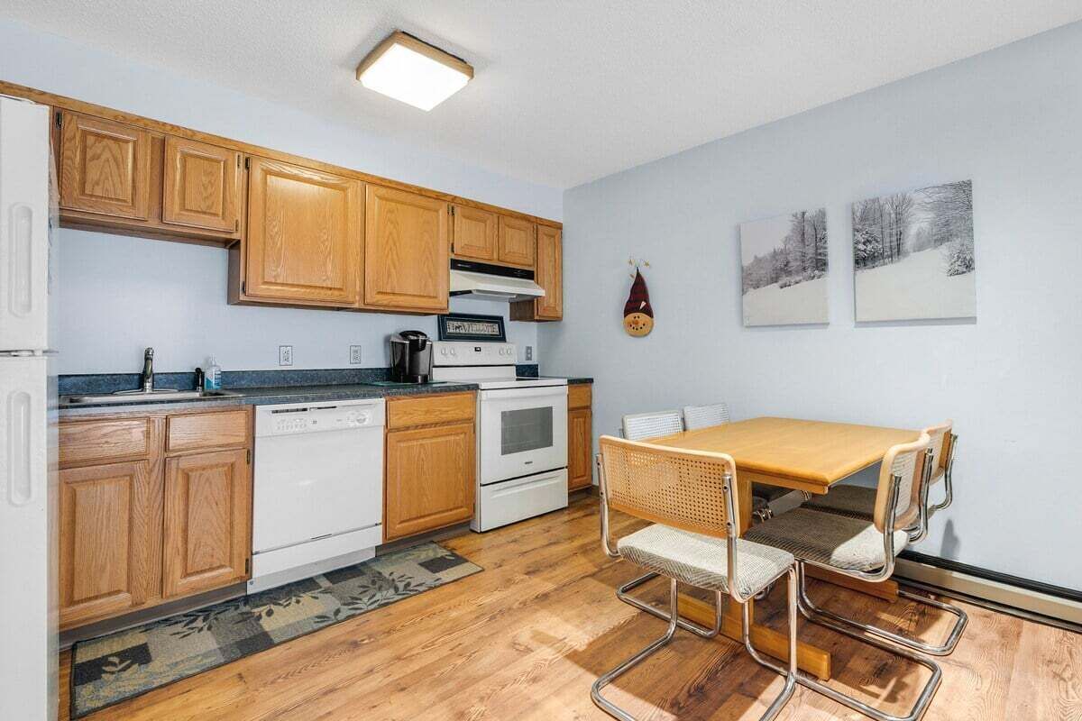 A compact kitchen with wooden cabinets, a stove, and a dining area with a table and chairs.