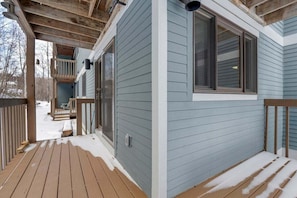 A covered wooden deck with a sliding glass door leading to a balcony.