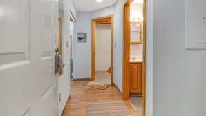 Un pasillo con una puerta blanca, suelo de madera, un tapete y un armario de madera.