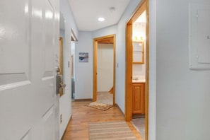 A hallway with a white door, wooden flooring, a rug, and a wooden cabinet.