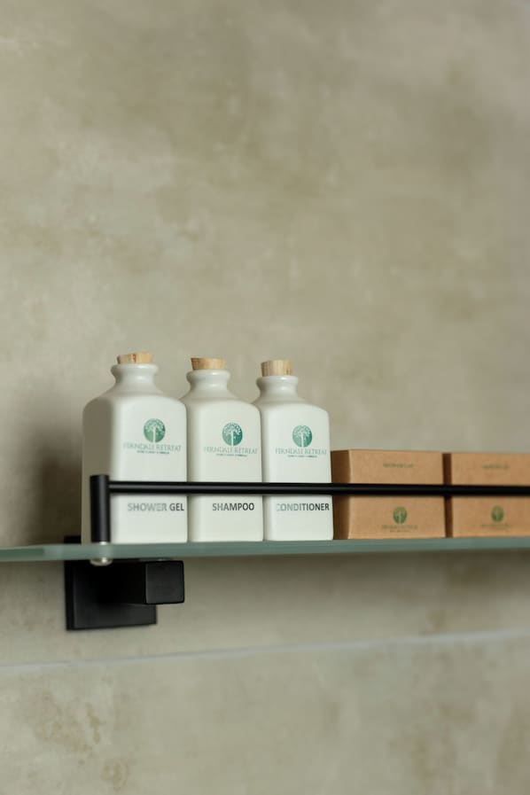 A shelf with three bottles labeled 'Shower Gel,' 'Shampoo,' and 'Conditioner,' and three boxes below them. - Ferndale Retreat (Rangala)