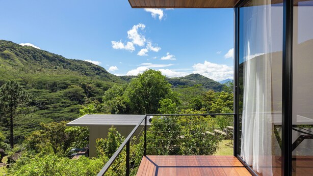 A balcony with a wooden ceiling overlooking a lush green landscape with hills and a clear sky. - Ferndale Retreat (Rangala)