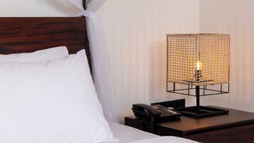 Un lit bien fait, avec du linge de lit blanc et une tête de lit en bois, une table de chevet avec une lampe et un téléphone.