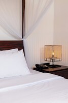 Una cama bien hecha con sábanas blancas y un cabecero de madera, una mesita de noche con una lámpara y un teléfono.