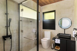 A modern bathroom with a glass shower enclosure, a toilet, a sink with a mirror, and a small trash bin. - Ferndale Retreat (Rangala)