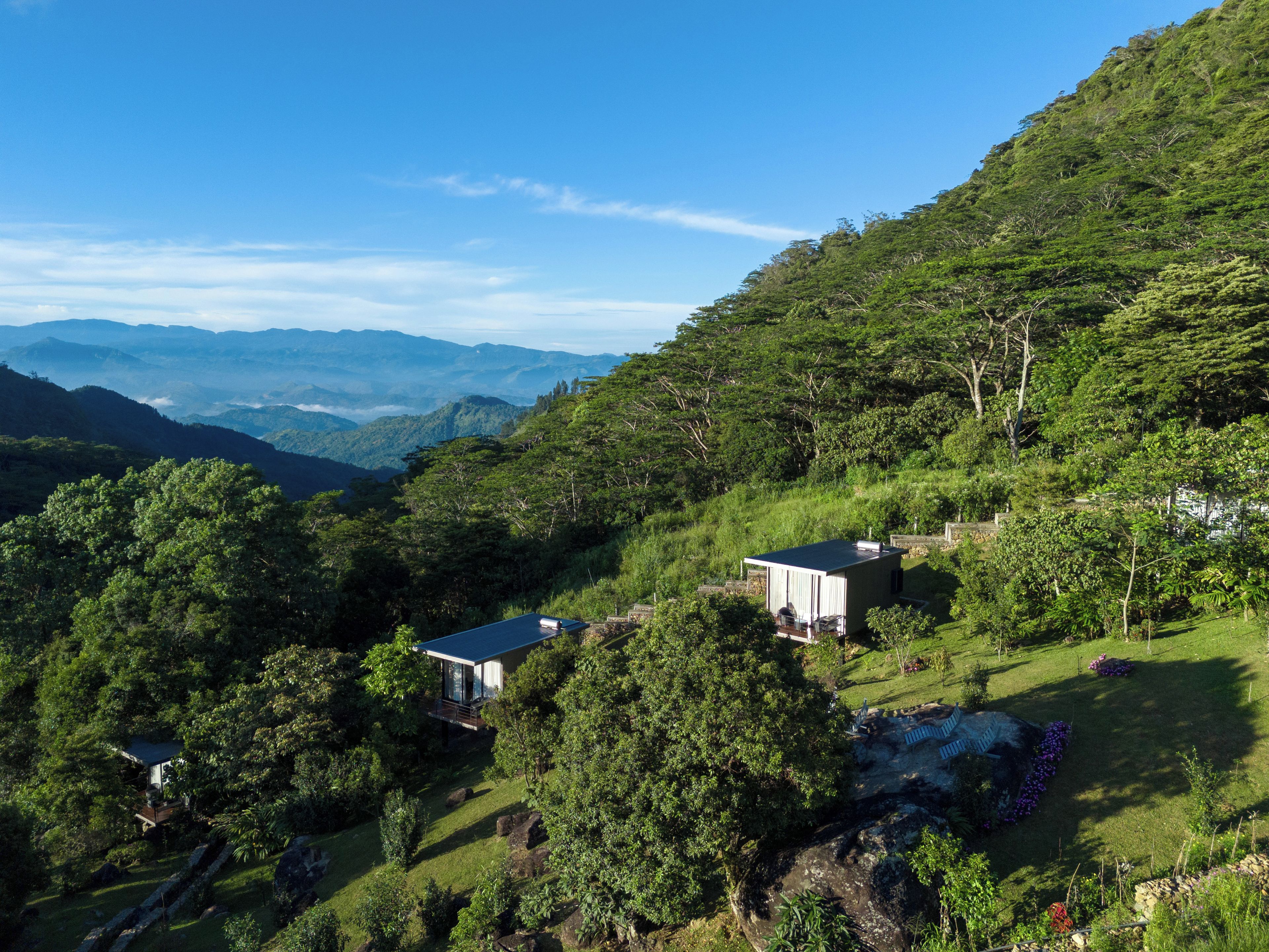 Une propriété située sur une colline, comprenant deux bâtiments modernes, une végétation luxuriante et une vue sur les montagnes lointaines.