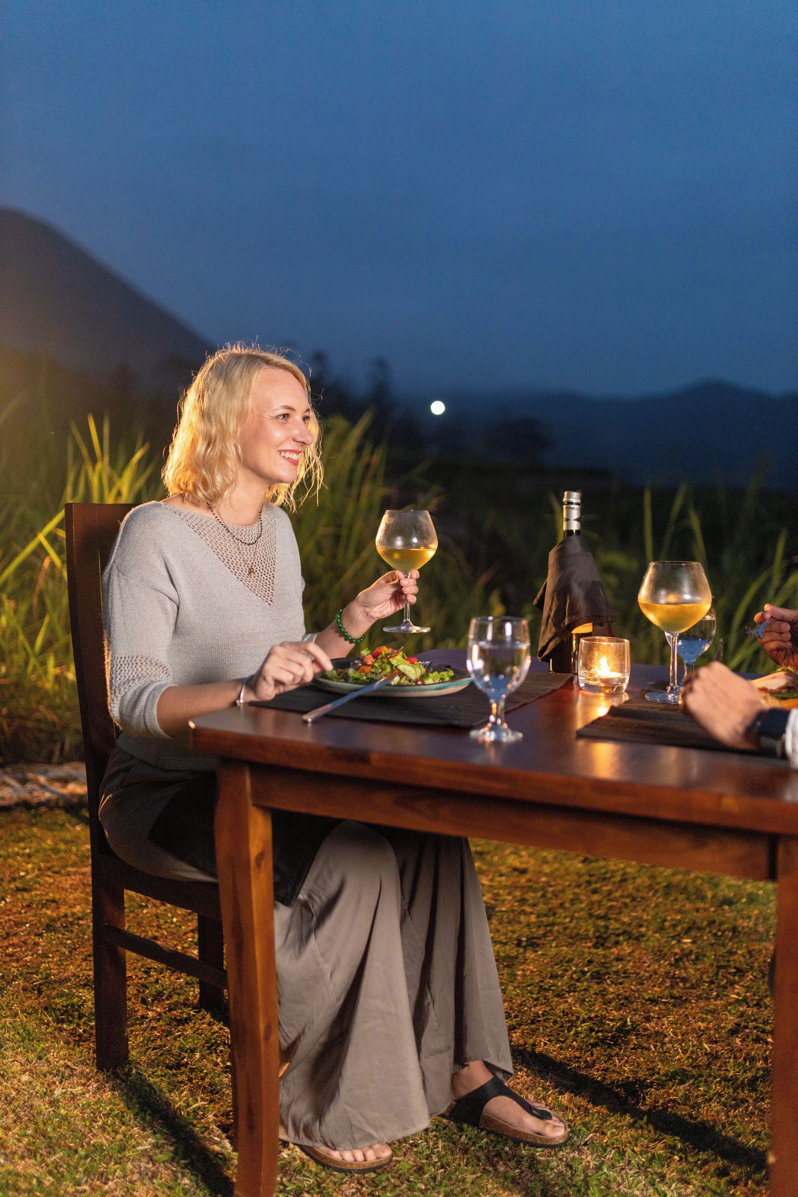 A dining table set outdoors with a bottle, glasses, and a candle.