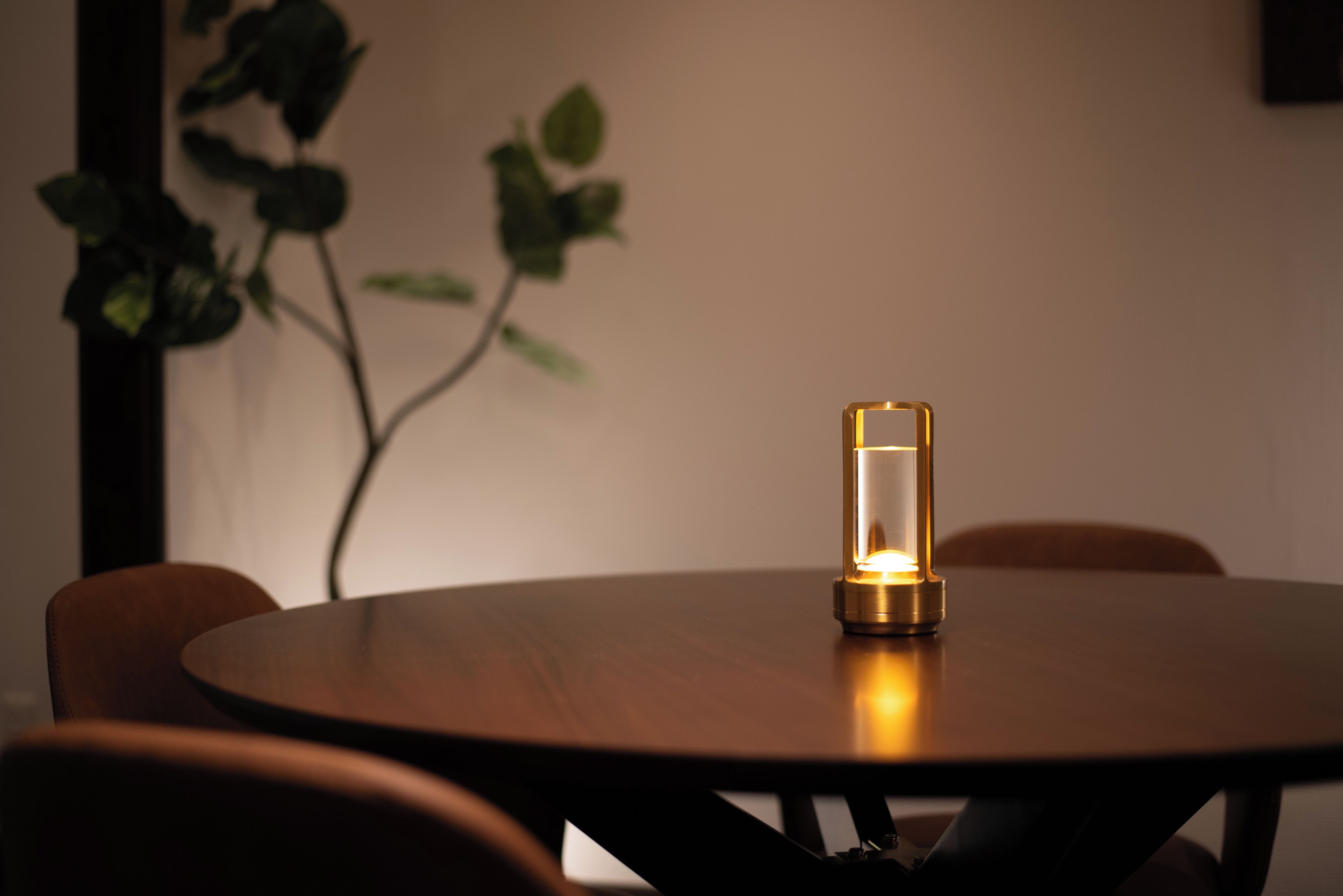 A round wooden table with a candle in a glass holder, surrounded by chairs.