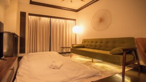 A hotel room with a bed, a green sofa, a standing lamp, and a wall-mounted fan. - Sunmallcrest306 (Tokyo)