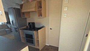 A compact kitchen with a refrigerator, stove, and wooden cabinets. - Donna 2 bed rhyl robin hood (Rhyl)
