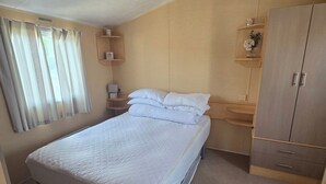 A compact bedroom with a single bed, a wooden wardrobe, a bedside table, and a window with curtains. - Donna 2 bed rhyl robin hood (Rhyl)