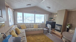 A compact living space with a sofa, a dining table, a TV, and a fan. - Donna 2 bed rhyl robin hood (Rhyl)
