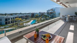 A balcony with a view of a swimming pool and modern buildings. - Newly Built 2 BDRM Modern Oasis w Gym & Pool (Estepona)