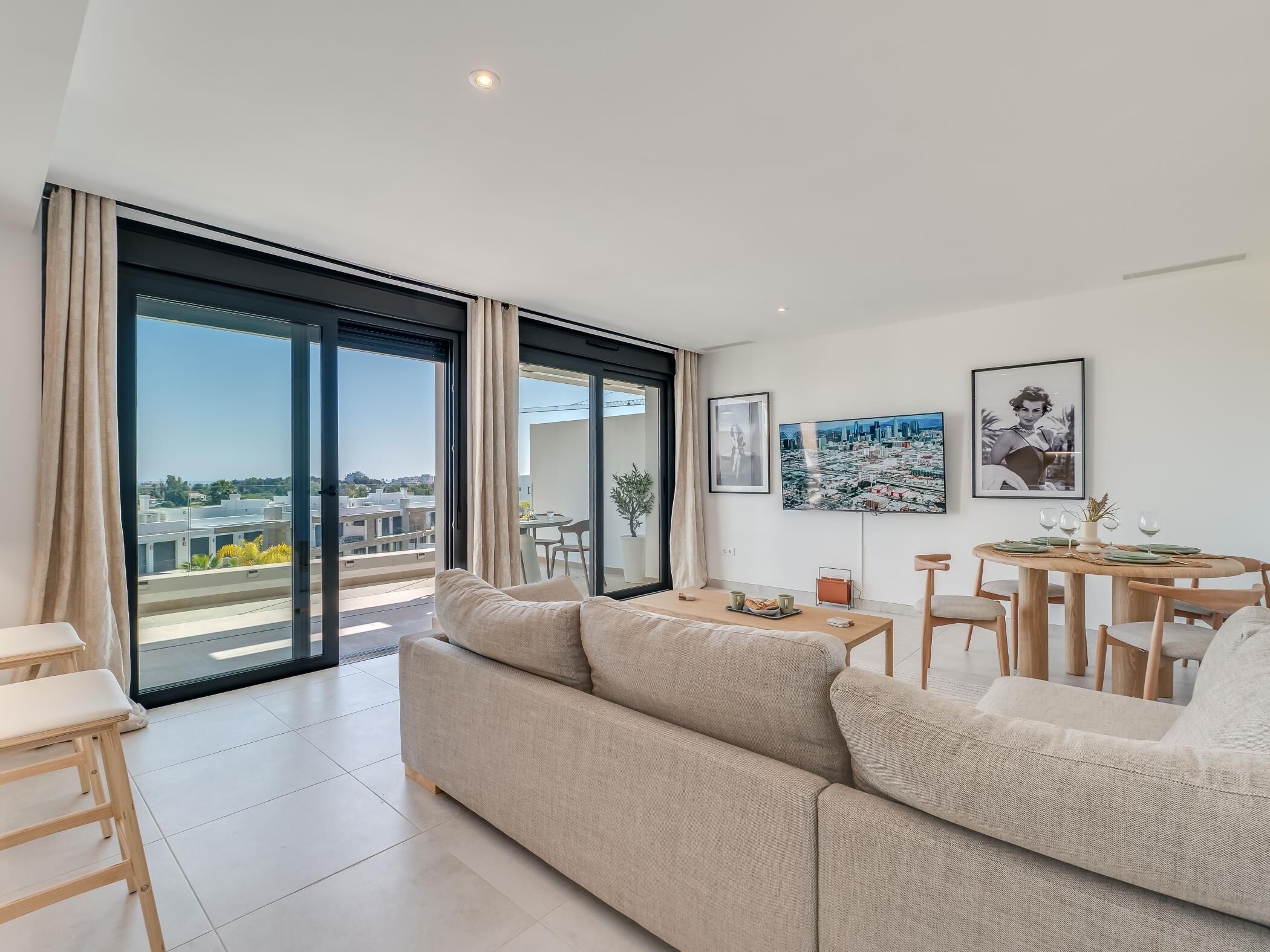 A modern living room with a large sofa, a dining table with chairs, and a cityscape view through floor-to-ceiling windows.