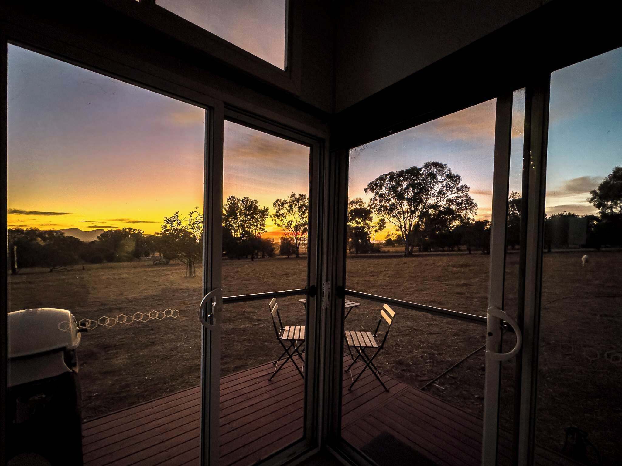 Une pièce dotée d’une porte vitrée donnant sur un espace extérieur avec vue sur un coucher de soleil et des arbres.