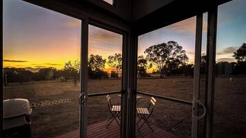 Ein Zimmer mit Glastür, die zu einem Außenbereich mit Blick auf Sonnenuntergang und Bäume führt.