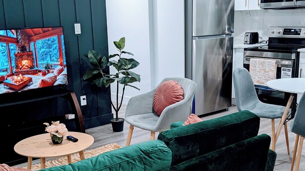 A modern living room with a green sofa, a round coffee table, and a TV displaying a fireplace scene.