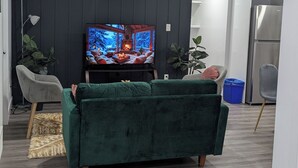 A modern living room with a green sofa, a flat-screen TV, and a dark wooden wall.