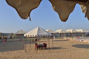 A desert setting with tents and a table with chairs under a canopy. - ACE Desert Resort (Jaisalmer)