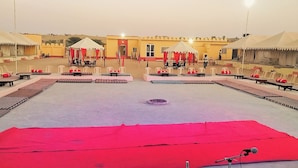 A spacious outdoor area with a central stage, surrounded by seating arrangements and tents. - ACE Desert Resort (Jaisalmer)