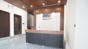 A reception area with a wooden counter, a marble wall, and patterned floor tiles. - Om Nilay Paying Guest House By GRB (Varanasi)
