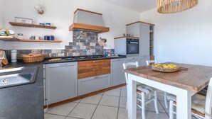 Une cuisine moderne avec des meubles gris, un plan de travail noir et une table à manger en bois avec des chaises.