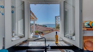 Une cuisine avec vue sur la mer, un évier et une bouteille d’huile d’olive.