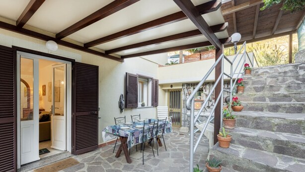 Un patio con piso de piedra, una mesa y sillas, una escalera con plantas en macetas y una puerta que da a un espacio interior.