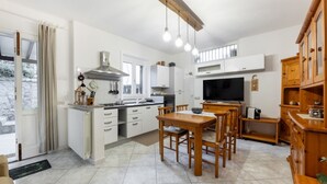 Una cocina moderna con armarios blancos, un comedor con mobiliario de madera y un televisor grande.