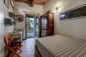 Ein Schlafzimmer mit einem Bett, einem Holzschrank, einem Heizkörper, einem Stuhl und einer Tür, die zu einem Garten führt.