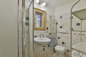 Ein Badezimmer mit Dusche, Waschbecken, Toilette und einem Fenster mit Blick auf Bäume.
