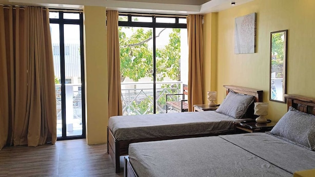 Ein Hotelzimmer mit zwei Betten, einem Balkon mit Vorhängen und Blick auf Grünflächen.