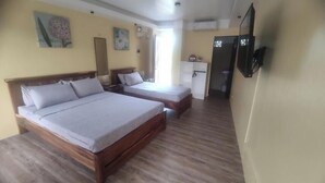 Ein Zimmer mit zwei Holzbetten, einer kleinen Küchenzeile und einem an der Wand befestigten Fernseher.