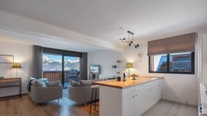 Una cuina moderna amb una illa central, una zona de menjador amb vista a les muntanyes i un espai d'estar acollidor amb un sofà i cadires.