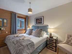 A bedroom with a bed, bedside lamp, and a small wooden side table. - Flambeaux B11 (CHATEL)