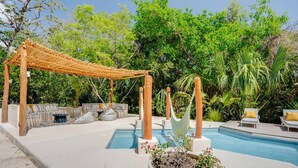 Een zwembadgedeelte met een houten pergola, buitenmeubels en weelderige begroeiing.